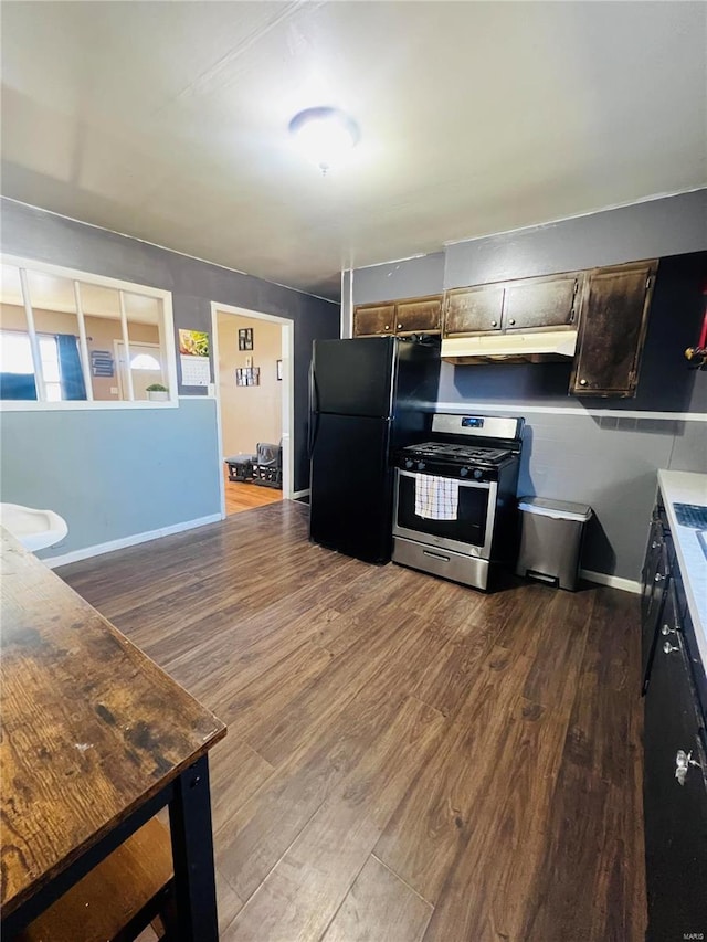 kitchen with under cabinet range hood, wood finished floors, baseboards, freestanding refrigerator, and gas stove