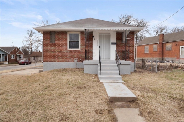 bungalow-style home with a shingled roof, a front yard, brick siding, and fence