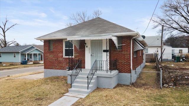 bungalow-style house featuring roof with shingles, fence, a front lawn, and brick siding