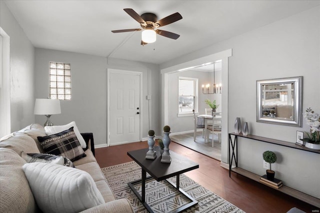 living area featuring ceiling fan with notable chandelier, wood finished floors, and baseboards