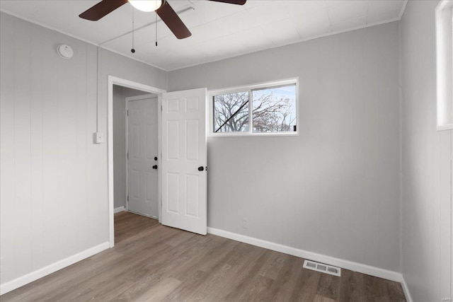 unfurnished bedroom featuring a ceiling fan, visible vents, baseboards, and wood finished floors