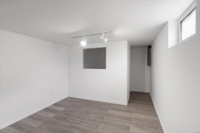 below grade area featuring track lighting, wood finished floors, and baseboards