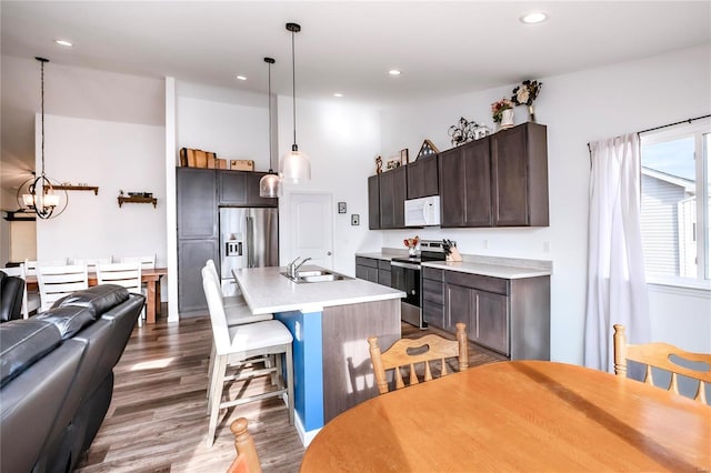 kitchen with light countertops, appliances with stainless steel finishes, open floor plan, a sink, and dark brown cabinets