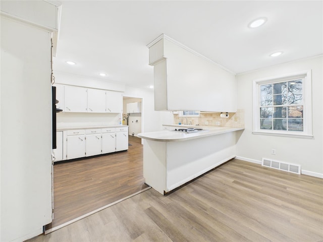 kitchen featuring light countertops, visible vents, white cabinets, wood finished floors, and a peninsula