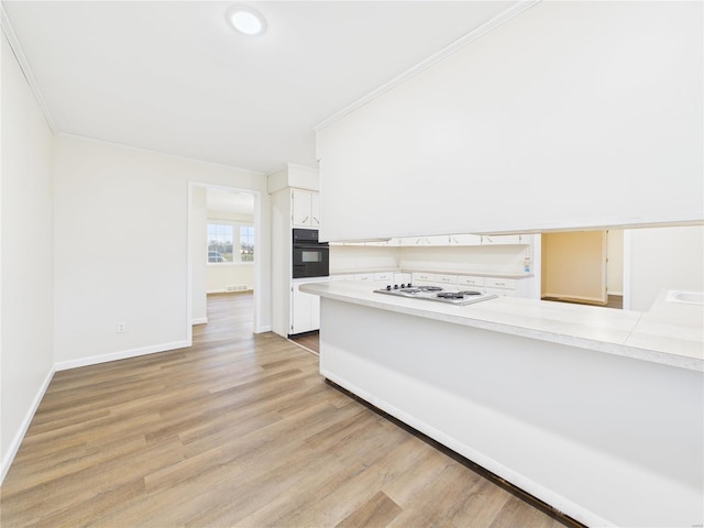 kitchen with white electric stovetop, light wood-style flooring, oven, light countertops, and crown molding