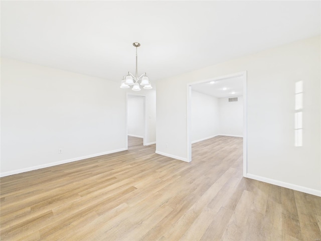 spare room with visible vents, light wood-style flooring, baseboards, and an inviting chandelier