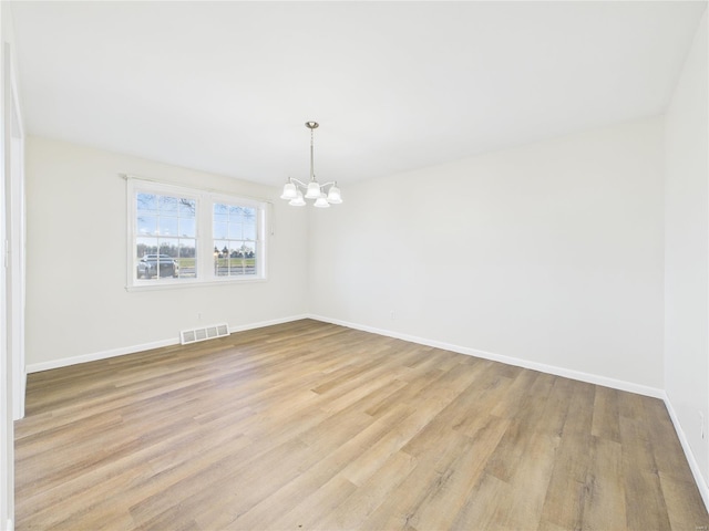 empty room featuring an inviting chandelier, light wood-style flooring, visible vents, and baseboards