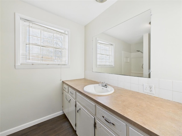 bathroom featuring baseboards, decorative backsplash, a shower, wood finished floors, and vanity