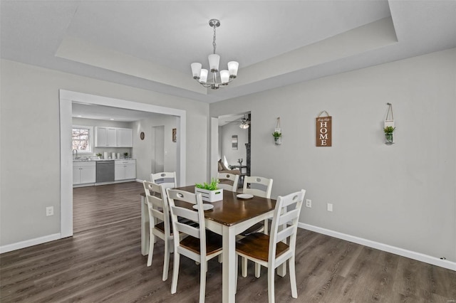 dining area featuring ceiling fan with notable chandelier, a tray ceiling, dark wood-type flooring, and baseboards