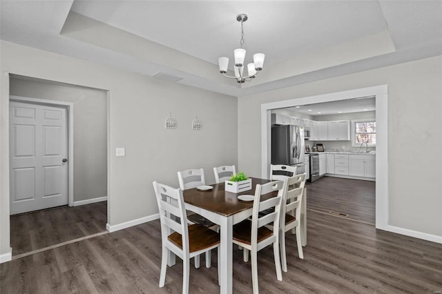 dining space featuring dark wood-type flooring, a tray ceiling, a chandelier, and baseboards