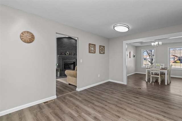 unfurnished dining area with a fireplace, a notable chandelier, visible vents, wood finished floors, and baseboards