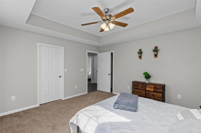 carpeted bedroom featuring baseboards, a tray ceiling, and ceiling fan