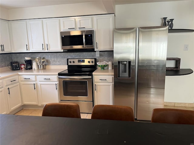 kitchen with tasteful backsplash, light countertops, stainless steel appliances, light tile patterned flooring, and white cabinetry