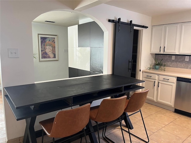 kitchen with light tile patterned floors, a barn door, stainless steel dishwasher, and white cabinets