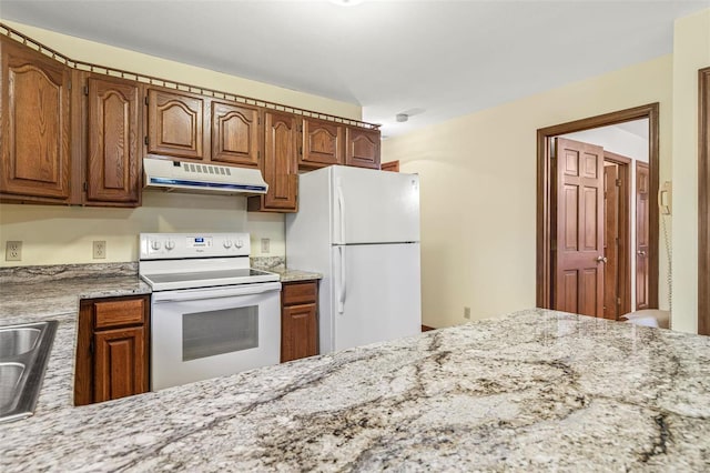 kitchen with white appliances, brown cabinetry, light stone countertops, under cabinet range hood, and a sink