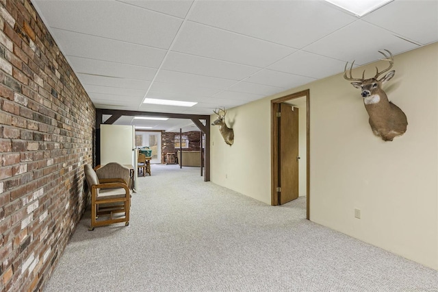 unfurnished room with brick wall, carpet flooring, and a drop ceiling