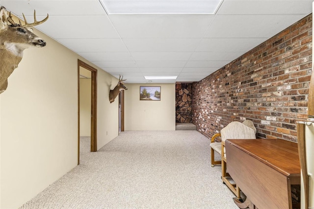 finished below grade area featuring brick wall, carpet flooring, and a paneled ceiling