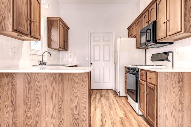 kitchen featuring a peninsula, a sink, light countertops, light wood-type flooring, and black appliances