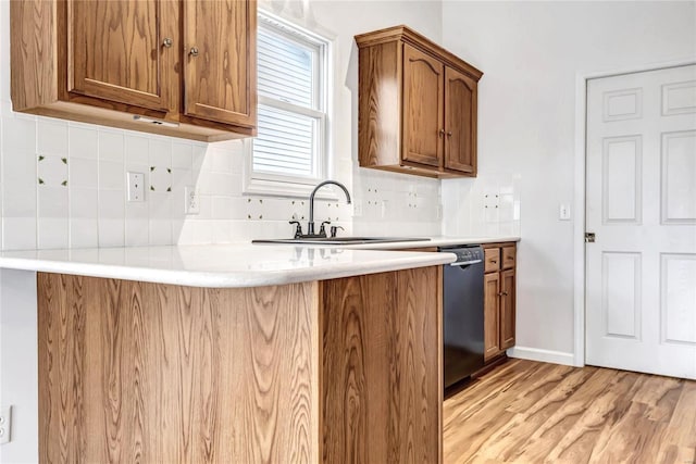 kitchen featuring decorative backsplash, brown cabinetry, dishwasher, light wood-type flooring, and a sink