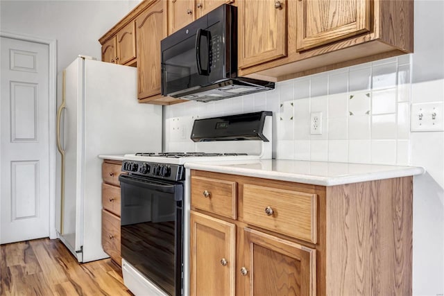 kitchen featuring tasteful backsplash, light countertops, black microwave, light wood-type flooring, and white range with gas stovetop