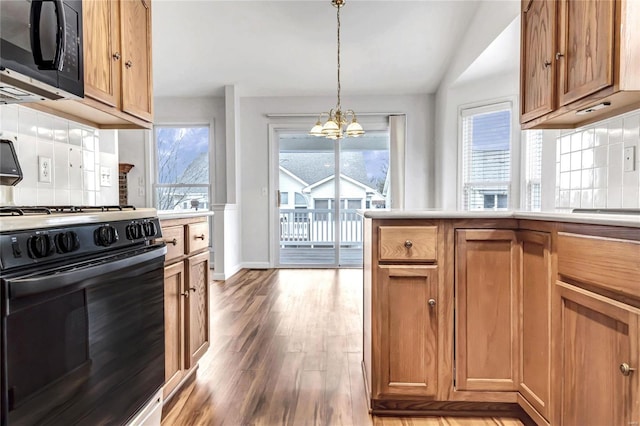 kitchen featuring brown cabinets, light countertops, wood finished floors, a chandelier, and black appliances