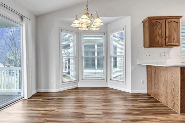 unfurnished dining area featuring lofted ceiling, baseboards, wood finished floors, and a notable chandelier