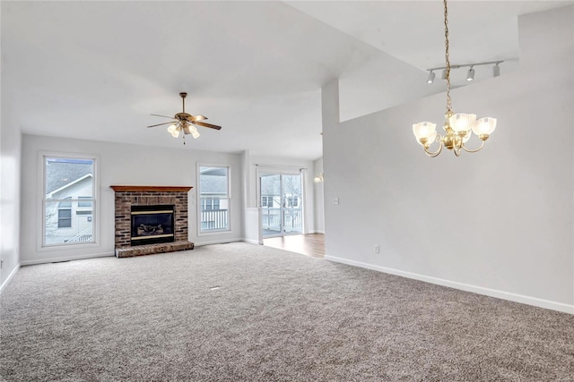 unfurnished living room featuring ceiling fan with notable chandelier, carpet floors, baseboards, vaulted ceiling, and a brick fireplace