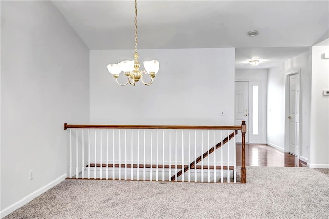 hallway with an inviting chandelier, baseboards, and carpet flooring