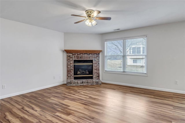 unfurnished living room featuring a ceiling fan, a brick fireplace, baseboards, and wood finished floors