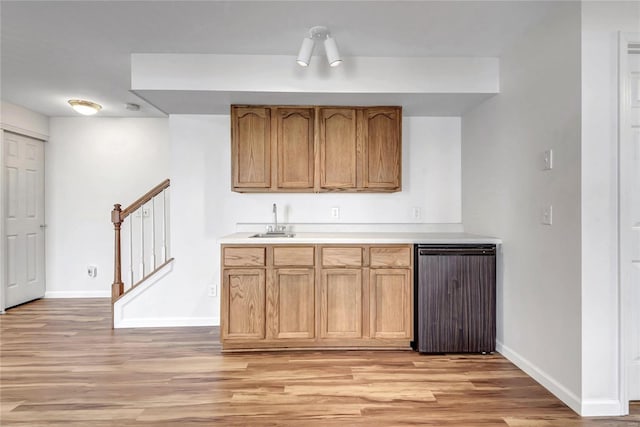 bar featuring light wood finished floors, baseboards, stairway, and a sink