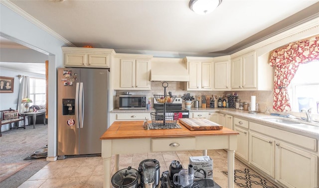 kitchen featuring a sink, wood counters, cream cabinets, stainless steel appliances, and custom exhaust hood