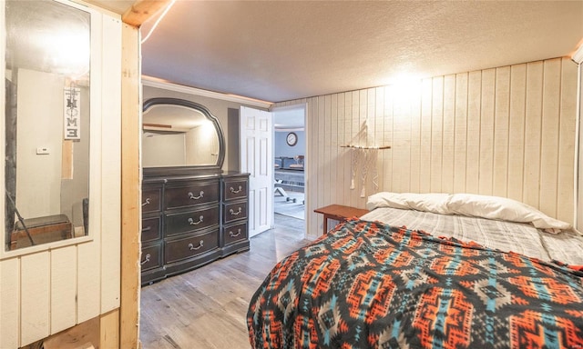 bedroom featuring wood walls, a textured ceiling, ornamental molding, and wood finished floors