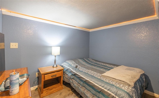 bedroom with a textured ceiling, wood finished floors, crown molding, and a textured wall