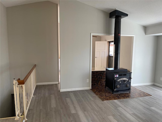 unfurnished living room featuring lofted ceiling, a wood stove, baseboards, and wood finished floors