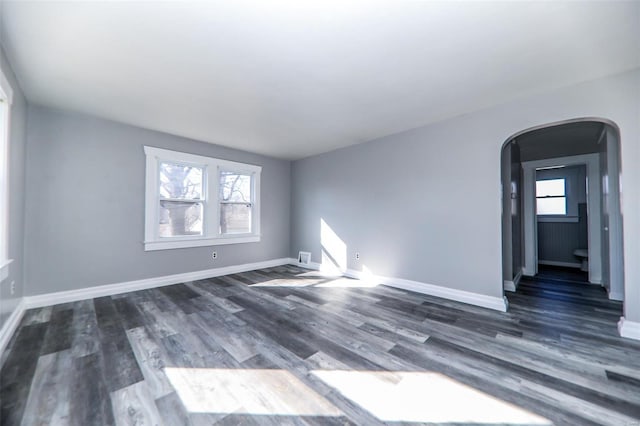 spare room featuring baseboards, arched walkways, dark wood-type flooring, and a wealth of natural light