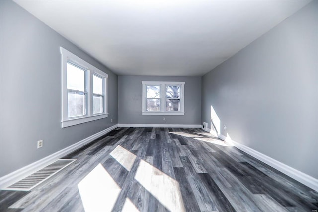 empty room featuring wood finished floors, visible vents, and baseboards