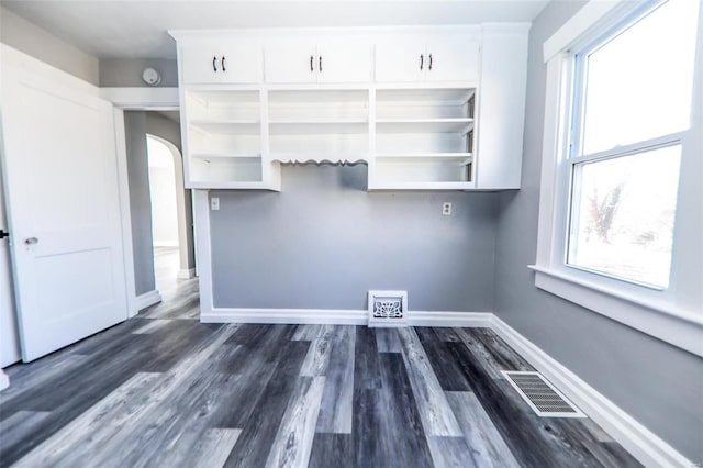 interior space with dark wood-style floors, baseboards, visible vents, and arched walkways