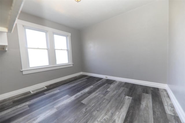 empty room with baseboards, visible vents, and dark wood finished floors