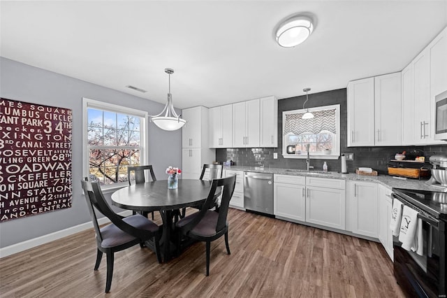 kitchen with wood finished floors, a sink, visible vents, appliances with stainless steel finishes, and decorative backsplash