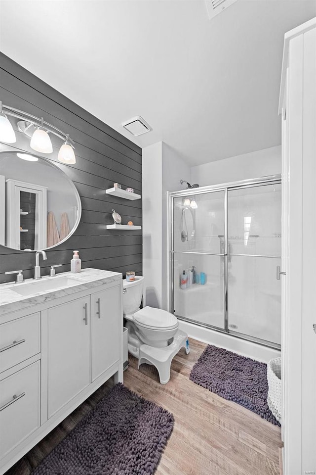 full bathroom featuring toilet, wood finished floors, visible vents, vanity, and a shower stall