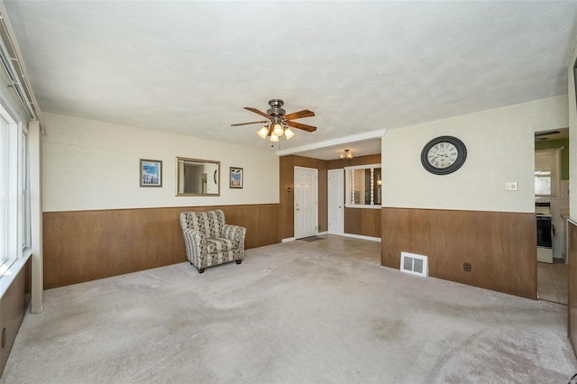 unfurnished room with visible vents, a ceiling fan, wainscoting, wood walls, and carpet flooring