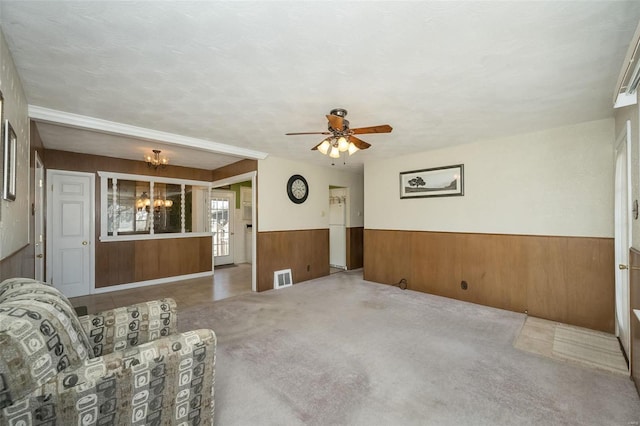 unfurnished living room featuring visible vents, a wainscoted wall, carpet floors, wood walls, and ceiling fan with notable chandelier