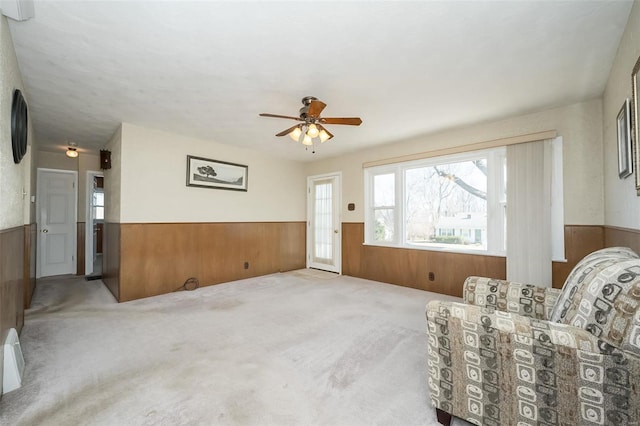 sitting room featuring carpet floors, wood walls, ceiling fan, and wainscoting