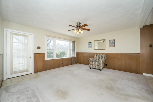 living area with a ceiling fan, wainscoting, wooden walls, and carpet flooring