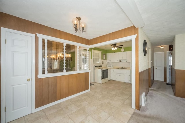 kitchen featuring wooden walls, white appliances, a sink, white cabinetry, and light countertops