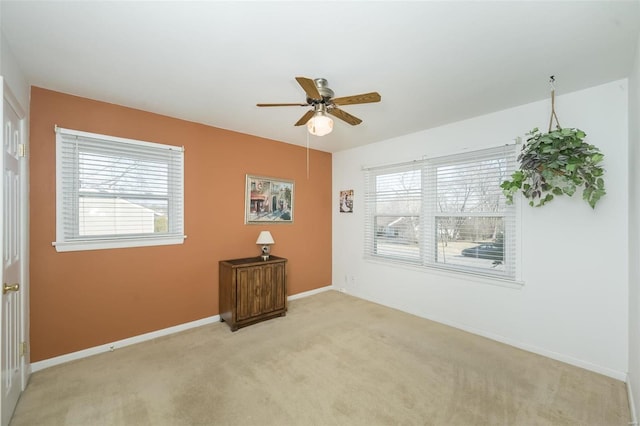 empty room with baseboards, plenty of natural light, a ceiling fan, and light colored carpet