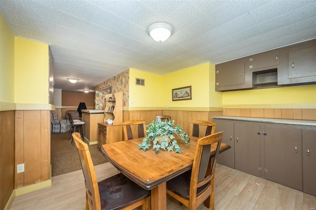 dining space with light wood-type flooring, wainscoting, visible vents, and wooden walls