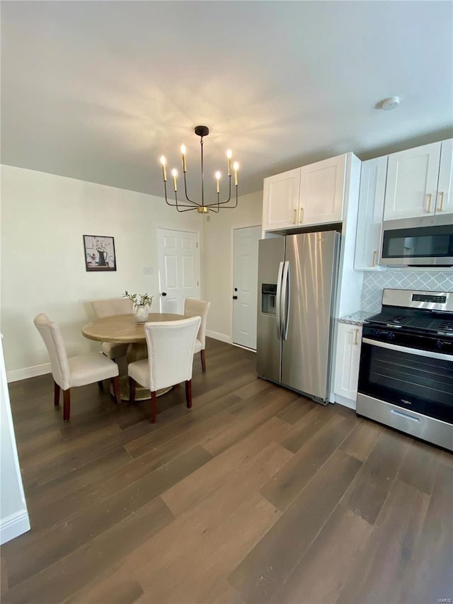 kitchen with dark wood-style floors, a notable chandelier, tasteful backsplash, appliances with stainless steel finishes, and white cabinetry