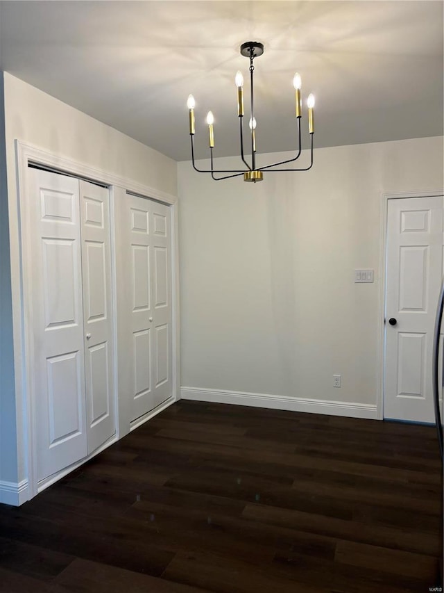 unfurnished dining area with a chandelier, dark wood finished floors, and baseboards