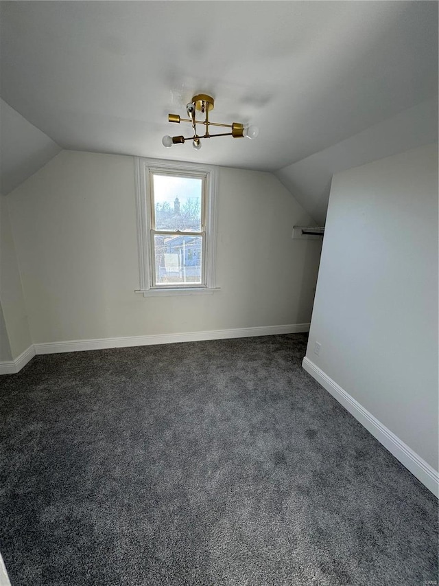 additional living space featuring vaulted ceiling, dark colored carpet, and baseboards